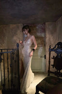 Woman in a sparkling silver dress standing in an ornate room with a chandelier.