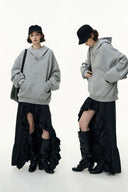 Person wearing a gray hoodie and black skirt with ruffled layers on a white background
