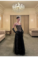 Woman in a black evening gown standing in an elegant room with a chandelier.