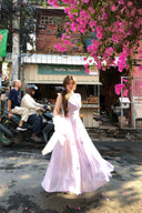 Woman in a pink dress standing on a street with pink flowers above her