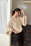 Side view of an ivory cowl-neck knit sweater showing the fitted ribbed hem and wide rabbit-fur-trimmed sleeves