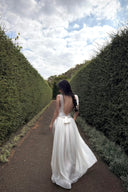 Woman in a Vogsion Amber Light Lace Spliced Open Back Tie Strap Maxi Dress walking along a path between hedges with a cloudy sky.