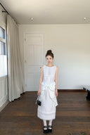 Woman in a Vogsion Shush TrongWhite Linen Statement Bow Petite Midi Dress standing in a room with wooden flooring and white walls.