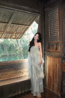 Woman in a light green  Vogsion Seraphina Tiered Chantilly Lace Maxi Dress standing inside a wooden structure with a view of water and trees outside.