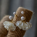 Pair of Vogsion Sculptural Petal & Lustrous Drop Earrings with white floral designs and pearl-like beads on a textured surface.