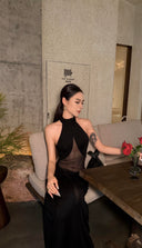 Woman in a Vogsion Noir Eclipse Sheer Halter Maxi Dress sitting at a table with a flower in a restaurant.