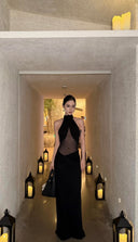 Woman in a Vogsion Noir Eclipse Sheer Halter Maxi Dress standing in a dimly lit hallway with lanterns.