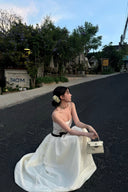 Woman in a Vogsion Élodie Lace Corset Bow Satin Maxi Dress sitting on a road with trees and buildings in the background