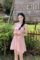 Woman in a Vogsion Odette Pearl-Trim Bubble Mini standing outdoors with greenery and a wooden sign in the background