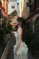 Woman in a Vogsion Pistachio Green Strapless Corset Ruffle Peplum Lace Prom Dress 2026 standing in an alleyway with buildings and plants around