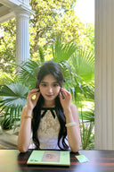 Woman in Vogsion Shush Trong Renaissance Stiff Wool-Lace Coquette Dress sitting at a desk with plants and a building in the background