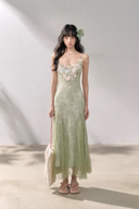 Woman wearing a light green dress with floral embellishments against a plain background
