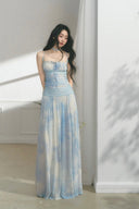 Woman wearing a light blue tie-dye dress standing in a softly lit room.