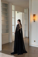 Vogsion Open Back Ribbon Maxi Dress – Elegant black pleated chiffon halter neck evening gown with dramatic sheer ribbon cape sleeves, open back cutouts, and flowing maxi skirt, worn by real Vogsion customer (not professional model) in luxury setting with global fast shipping