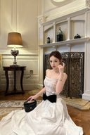 Woman in a Vogsion Élodie Lace Corset Bow Satin Maxi Dress with a black bow sitting in a room with decorative elements.