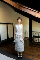 Woman in a Vogsion Shush TrongWhite Linen Statement Bow Petite Midi Dress standing in a room with wooden floors and a staircase.