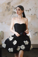 Woman in a Vogsion Midnight Bloom Architectural Mini Dress with floral embellishments sitting against an artistic wall.