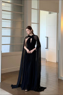 Vogsion Open Back Ribbon Maxi Dress – Elegant black pleated chiffon halter neck evening gown with dramatic sheer ribbon cape sleeves, open back cutouts, and flowing maxi skirt, worn by real Vogsion customer (not professional model) in luxury setting with global fast shipping