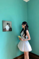 Woman in a Vogsion Shush Trong Renaissance Stiff Wool-Lace Coquette Dress standing in a room with teal walls, looking at a painting.