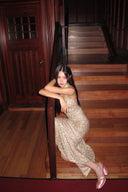 Woman in a Vogsion Champagne Gold Cross-Strap Backless Mermaid Maxi Dress sitting on wooden stairs