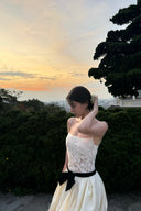 Woman in a Vogsion Élodie Lace Corset Bow Satin Maxi Dress with a black belt standing outdoors with trees and sunset in the background