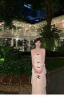 Woman in a Vogsion Élodie Bow-Tiered Ivory Lace Maxi Dress standing in a garden with a building in the background