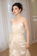 Woman in a Vogsion 2026 3D Blooming Rose Strapless Ruched Pleated Wedding Dress with pearl jewelry against a neutral background