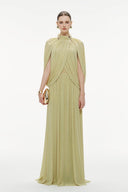 Woman wearing a Vogsion Light Pomelo Olive Mesh Knit Draped Cape Pleated Maxi Dress with a cape on a white background
