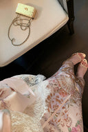 Close-up of a person wearing Vogsion Adorned in Aranjuez Bias Cut Slipdress and high-heeled shoes, with a handbag on a chair in the background.