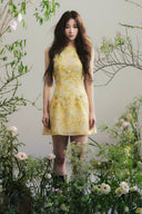 Vogsion Aurelia Soleil Floral Mini Dress worn by a normal customer in a botanical studio, high-end A-line silhouette, luxury yellow floral fashion, authentic customer photo.