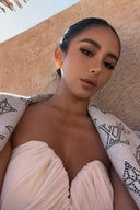 Woman lying on a patterned blanket against a beige wall, wearing Vogsion ivory strapless cut out ruched maxi dress