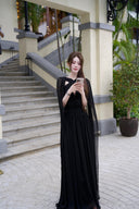 Vogsion Open Back Ribbon Maxi Dress – Elegant black pleated chiffon halter neck evening gown with dramatic sheer ribbon cape sleeves, open back cutouts, and flowing maxi skirt, worn by real Vogsion customer (not professional model) in luxury setting with global fast shipping