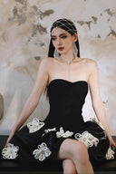 Woman in a Vogsion Midnight Bloom Architectural Mini Dress with white floral details sitting against a textured wall.