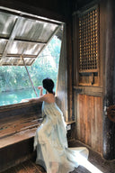 Woman in a light green Vogsion Seraphina Tiered Chantilly Lace Maxi Dress sitting on a wooden boat looking out at water.