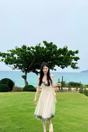 Woman in a Vogsion "Lucienne" Ethereal Tulle & Contrast Lace-Inset Midi Dress standing on a grassy area with a scenic background of trees and water.