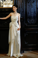 Woman in Vogsion 2026 3D Blooming Rose Strapless Ruched Pleated Wedding Dress standing in an elegant room with dark wood paneling.