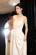 Woman in a Vogsion 2026 3D Blooming Rose Strapless Ruched Pleated Wedding Dress with jewelry, standing indoors.
