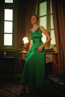 Woman in a green dress standing in a room with curtains and a lamp.