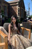 Woman wearing the VOGSION Luna Twist Midi Dress in Cream Perla Paisley silk-linen fabric, featuring a voluminous flare skirt and waist cut-out in a lush garden setting