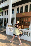 Woman in a Vogsion Velvandis Off Shoulder Dot Mini Dress sage green polka dot and straw hat walking in front of a building with a sign.