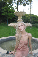 Woman in a Vogsion Strapless Twist Knot Satin Draped Maxi Dress sitting by a fountain in a garden