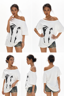 Petite model wearing the VOGSION ÉCLIPSE oversized white off shoulder graphic tee with abstract eye print. Breathable cotton loose fit summer t-shirt designed for petite women with a flattering off shoulder neckline that can also be worn as a boat neck, perfect for casual streetwear, travel, layering and everyday outfits.