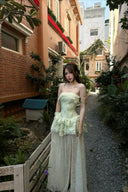 Woman in a Vogsion Pistachio Green Strapless Corset Ruffle Peplum Lace Prom Dress 2026 standing in an urban alleyway with buildings and plants around.