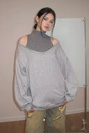 Person wearing a gray oversized sweater with a high collar and light-colored pants in an indoor setting.