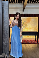 Woman in a blue dress standing in a room with a painting on the wall.