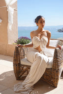 Woman in Vogsion ivory strapless cut out ruched maxi dress sitting on a wicker chair by the sea.