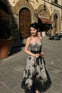 Vogsion Seraphina Floral Bustier Dress from the Kindred Spirit Spring 2026 collection, featuring a white and black botanical floral print, beaded straps, and a tie-waist, worn by a Vogsion customer in a historic European plaza