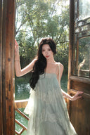 Woman in a light green Vogsion Seraphina Tiered Chantilly Lace Maxi Dress standing in front of a wooden door with a garden view.