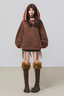 Person wearing a brown hoodie with fringe details and matching knee-high boots on a plain background