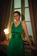 Woman in a green dress standing in a room with patterned curtains and a lamp.